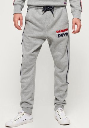 Graue Sweatpants mit elastischem Bund und Kordelzug. Mit roten und marineblauen Stickereien "SUPERDRY" und "DRY" am linken Oberschenkel. Mit seitlichen Streifen.