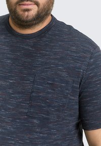 Marineblaues T-Shirt mit kurzen Ärmeln aus strukturiertem, mehrfarbigem Stoff. Verfügt über eine kleine Brusttasche und einen klassischen Rundhalsausschnitt.