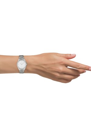 Montre-bracelet en métal argenté avec un cadran rond blanc, des repères minimalistes et un bracelet à maillons, portée sur un poignet humain.