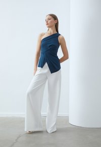 Navy blue, one-shoulder top with wrapped design and side knot detail, paired with white, wide-leg trousers. Smooth fabric texture.