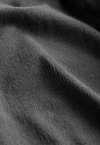 Tissu noir à texture lisse, présentant des motifs tissés subtils et des plis délicats. La surface semble légèrement réfléchissante à la lumière.