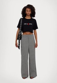 Fekete, rövidített póló "THE ROPES" felirattal és piros szívvel. Magas derekú, széles szárú, fekete-fehér kockás nadrág. Fekete pántos táska, lapos szandálok.