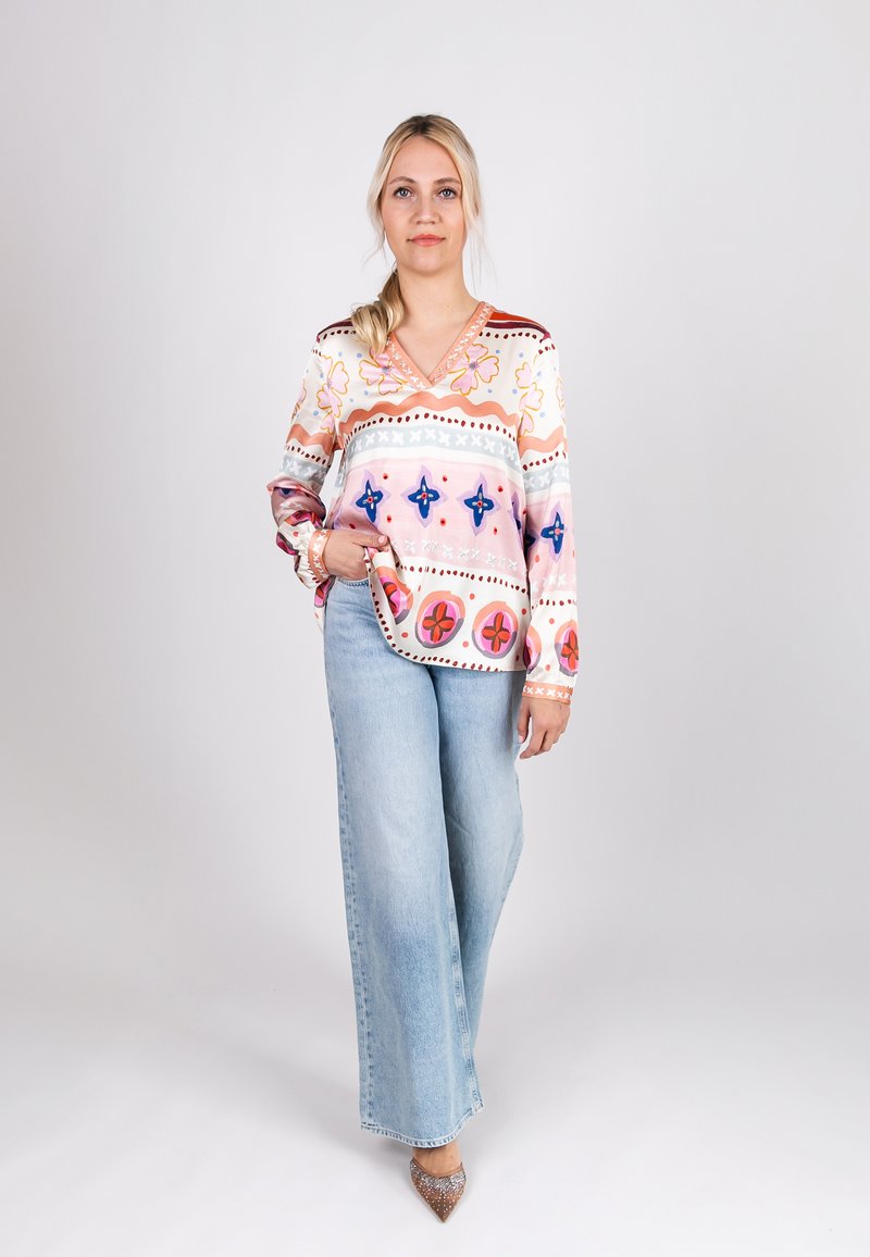 Long-sleeve blouse in pastel colors with floral and geometric patterns, paired with light blue wide-leg jeans and pointed heels.