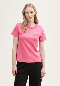 Rosa bomullströja med korta ärmar och rund halsringning, med en liten orange grafisk design på bröstet.
