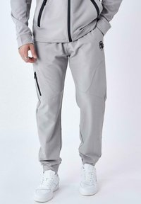Pantalones deportivos de color gris claro, hechos de una tela suave, con bolsillos laterales con cremallera, detalles cosidos y puños elásticos en los tobillos.