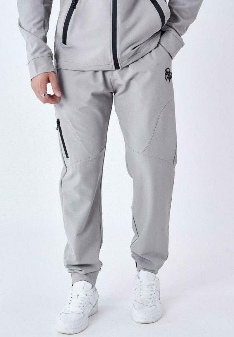 Pantalones deportivos de color gris claro, hechos de una tela suave, con bolsillos laterales con cremallera, detalles cosidos y puños elásticos en los tobillos.