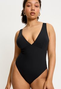 Maillot de bain une pièce noir avec un décolleté en V profond, des bretelles larges et des jambes échancrées, fabriqué en tissu lisse et extensible.