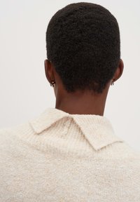 Maglione crema a maniche corte con finitura testurizzata, dotato di colletto a risvolto e cuciture visibili all'altezza del collo.