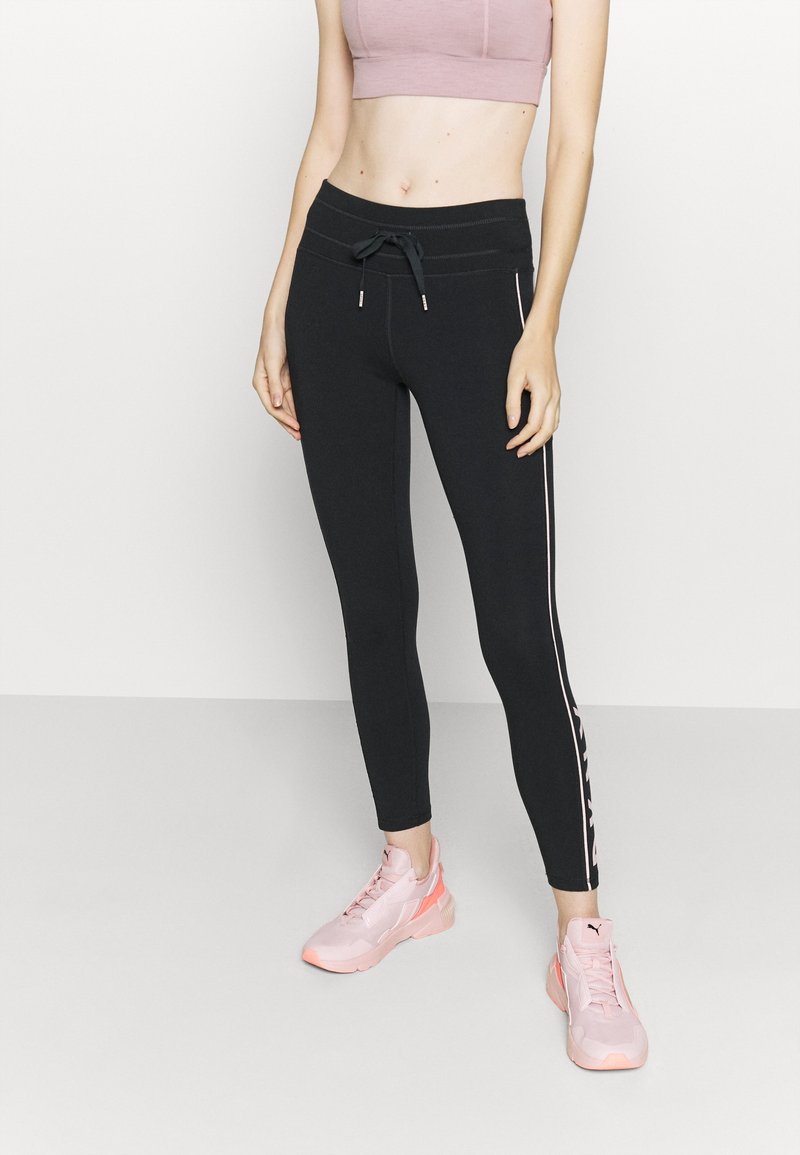 Černé sportovní legíny s úzkým střihem, se postranními pruhy a elastickým pasem na šňůrku. V kombinaci se světle růžovými teniskami a zkráceným topem.