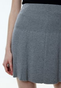 Femme portant une jupe en tricot côtelé grise taille haute avec un ourlet festonné, associée à un haut noir, main détendue sur le côté.