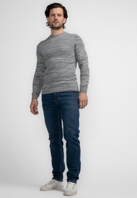 Grauer Langarmpullover mit strukturiertem, meliertem Muster, getragen mit dunkelblauen Jeans und weißen Sneakers. Schlichtes Rundhalsdesign und figurnaher Schnitt.