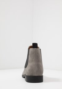 Botín Chelsea de ante gris con paneles laterales elásticos y una lengüeta. Suela de goma negra plana con un acabado suave y mate.