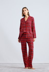 Rød ternet pyjamas sæt med en knap-op top og matchende bukser, lavet af blødt stof. Designet inkluderer en krave og lige snit.