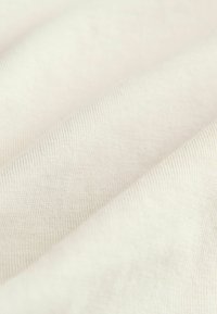 Ljust beige bomullstyg med en jämn yta, som har subtila ribbade mönster och mjuk drapering, vilket skapar mjuka veck och skuggor.