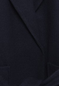 Marineblauer Wollmantel, doppelt knöpfbares Design, weiche Textur, mit breiten Revers und zwei vorderen Taschen, ausgestattet mit einem passenden Stoffgürtel.