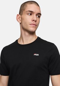T-shirt di cotone nero con colletto rotondo e un piccolo logo Fila bianco e rosso sul lato sinistro del petto. Maniche corte, texture liscia.