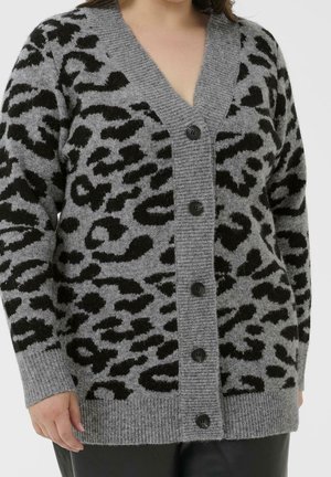 Cardigan gris boutonné avec imprimé léopard noir porté sur un pantalon noir, montré des épaules aux hanches.