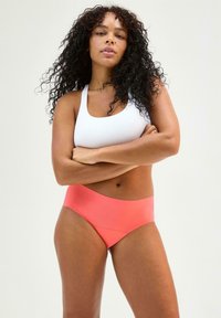 Bra sportivo bianco a coste abbinato a bikini a vita alta in corallo liscio. Il tessuto ha una texture elastica, offrendo una vestibilità aderente.