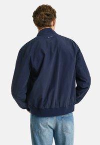 Giacca bomber blu navy con orlo a coste, polsini elasticizzati e un logo sul retro. Realizzata in tessuto liscio, presenta una vestibilità casual.