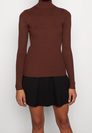 Bruine geribbelde turtleneck top met lange mouwen, gecombineerd met een zwarte rok. De top heeft een strakke pasvorm en een zachte textuur.