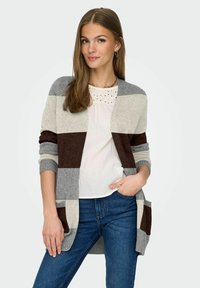Lange cardigan in grijs, romig en bruine strepen, met ribgebreide manchetten en zakken, gedragen over een wit topje en blauwe jeans.