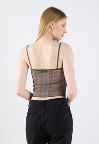 Brūns šaha raksta cropped topiņš ar plānām siksnām, ar pārbaudītu rakstu un pieguļošu dizainu. Apvienots ar augsto vidukli melnajām džinsa biksēm.