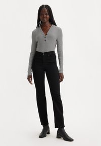 Top de manga larga a rayas con botones en blanco y negro, combinado con jeans negros de talle alto. Modelo lleva botas de tacón negro al tobillo.