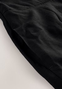 Section de tissu noir avec des coutures visibles et une couture, montrant la texture et les plis sur un fond clair.