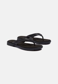 Black flip-flops with a textured footbed, rubber sole, and a sleek strap design. Features stitching accents on the strap.