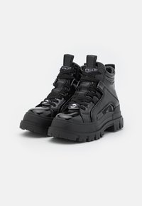 Zapatillas altas negras con un acabado brillante, que cuentan con suelas de goma gruesas, acentos texturizados y cordones negros. Detalle del logo prominente en la lengüeta.