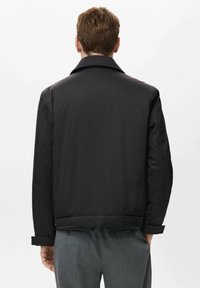 Chaqueta bomber negra con cuello plano, ajuste clásico y puños abotonados. Tejido suave con un diseño limpio y detalles minimalistas.