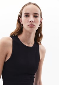 Top senza maniche nero con una texture a coste, caratterizzato da un collo rotondo e un design aderente, abbinato a orecchini a cerchio argentati.