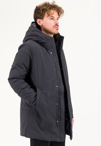 Parka grigia scura isolata con cappuccio, chiusura a zip, bottoni a pressione e tasche laterali, con un esterno liscio e resistente all'acqua.