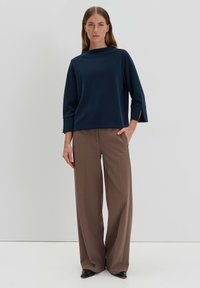 Navy blue boat-neck top with 3/4 sleeves and side slits, paired with high-waisted brown wide-leg trousers and black pointed shoes.