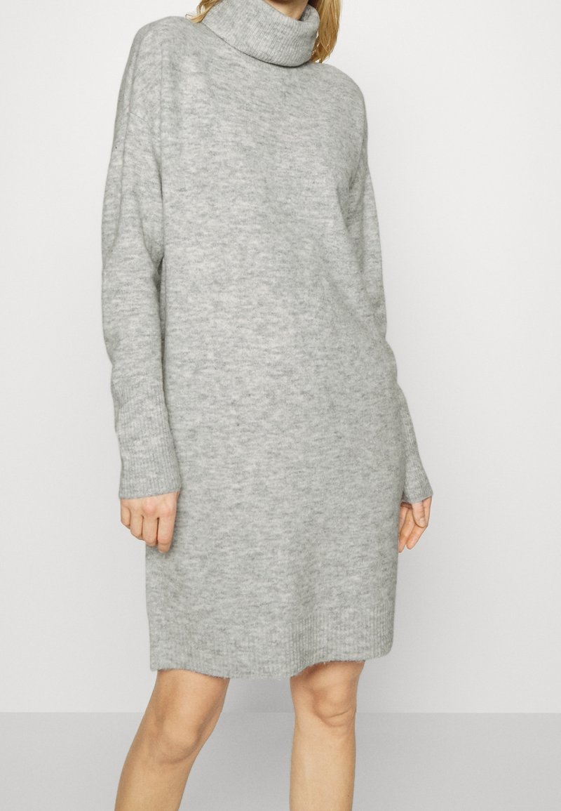 Robe-pull grise avec un col roulé haut, des manches longues et des poignets côtelés. Texture douce avec une coupe décontractée, se terminant au-dessus des genoux.