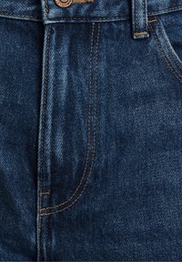 I jeans in denim presentano un colore blu scuro con cuciture in vista, un bottone metallico e tasche anteriori. Il tessuto ha una texture e una finitura classiche.
