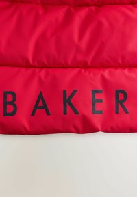 Röd puffjacka med en mjuk, glänsande yta med ordet "BAKER" i fet svarta bokstäver över bröstet.