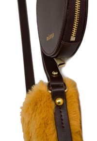 Brown leather crossbody bag featuring a round zippered compartment, yellow faux fur accent, gold hardware, and a textured strap.