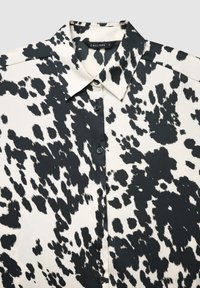 Blusa a maniche corte con motivo bianco e nero, collo classico e bottoni sul davanti, realizzata in tessuto liscio dalla texture morbida.