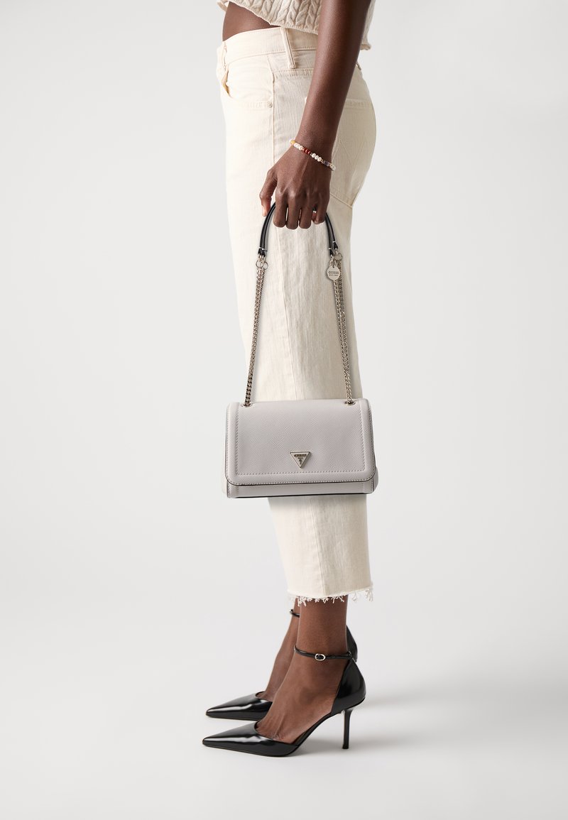 Grå teksturert håndveske med kjede-rem og logo detaljer, kombinert med hvite cropped bukser og svarte patent stilettos med ankelstropper.