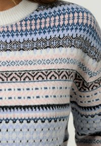 Sweter dzianinowy z okrągłym dekoltem i wielokolorowymi wzorami geometrycznymi w odcieniach niebieskiego, różowego i czarnego na białym tle. Miękka tekstura.