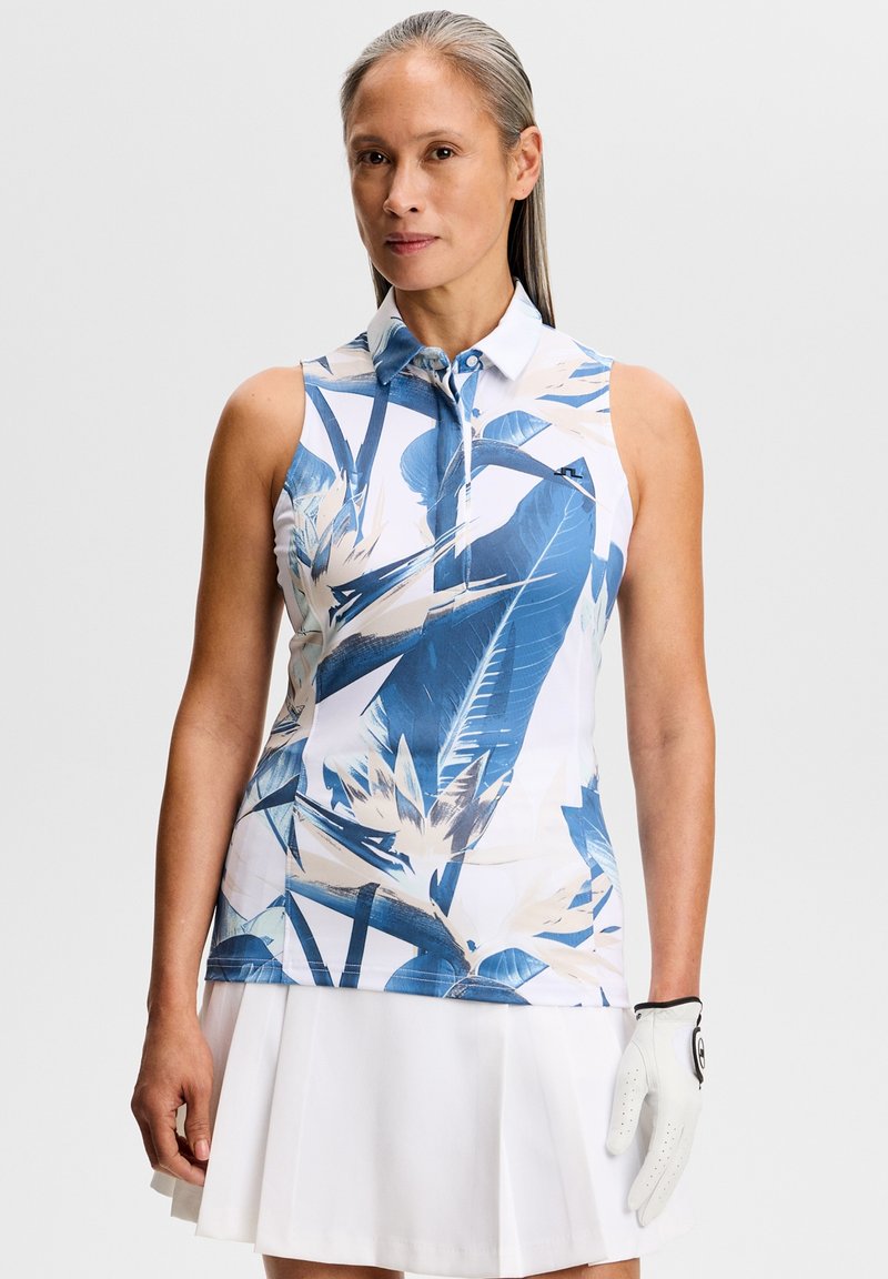 Polo senza maniche con motivo di foglie tropicali blu e bianche, dotata di colletto e chiusura con bottoni. Indossata con una gonna da tennis bianca e un guanto.