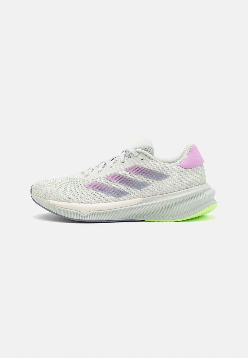 Baskets de sport gris clair avec des rayures lavande, languette rose au talon, lacets blancs, et semelle blanche et vert néon sur fond uni.