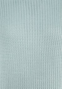 Ljusblå stickad tröja med ett strukturerat mönster, som har en lös väv och mjuk yta, med jämna stygn genom hela plagget.