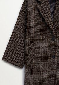 Manteau en laine à carreaux marron et noir avec deux boutons noirs et larges revers, présenté de l'épaule à la taille sur fond blanc.