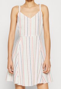 Gestreiftes Kleid mit V-Ausschnitt, verstellbaren Spaghettiträgern und ausgestellt Rock. Farbige Streifen in Rot, Blau und Grün auf weißem Hintergrund.