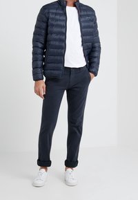 Navy puffer jacket with horizontal quilting, front zipper, paired with white t-shirt and dark pants, completed by white sneakers.