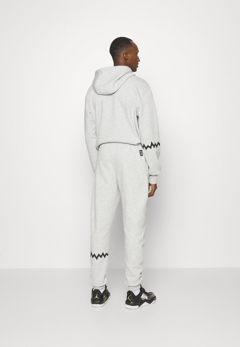 Felpa grigia in cotone con un design cropped e dettagli a zigzag neri sulle maniche, abbinata a pantaloni jogger grigi che presentano dettagli a zigzag simili.