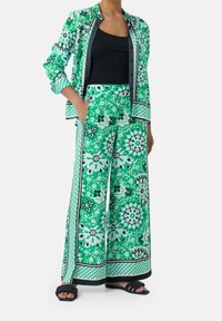 Blouse à motifs floraux verts et pantalon à jambes larges avec accents noirs. Tissu léger, chemise à boutons et poches sur le pantalon.