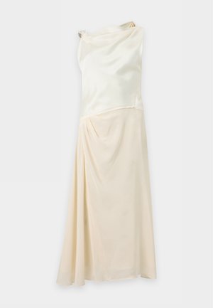 Une femme présente un haut sans manches couleur ivoire et une jupe midi, avec un sac à main bordeaux et des talons à brides, sur un fond uni.